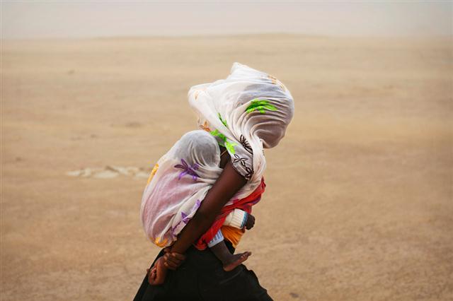 Một người phụ nữ cõng đứa con trên lưng và che khăn choàng lên mặt đi qua một trận bão cát ở Timbuktu