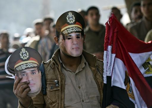 Một người bán dạo cờ Ai Cập và mặt nạ mang chân dung của Tổng Abdel Fattah al-Sisi xếp hàng bên ngoài một trạm bỏ phiếu trong ngày thứ hai của cuộc trưng cầu trên một hiến pháp mới