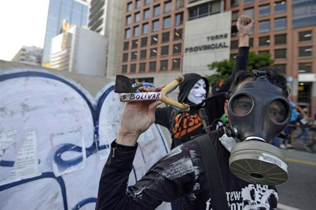 Một người đàn ông đeo mặt nạ vung chiếc ná gỗ ghi chữ S.Bolivar trong một cuộc biểu tình chống lại chính phủ của Nicolas Maduro tại Caracas