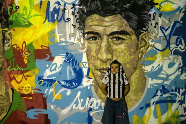 Một cậu bé đứng trước bức tường vẽ chân dung của cầu thủ bóng đá nổi tiếng Tavares Bastos Favela tại Rio de Janeiro, Brazil
