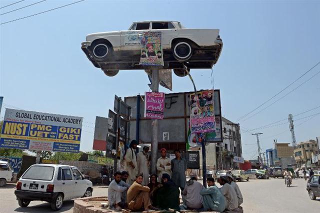 Công nhân Pakistan ngồi trong bóng râm của một chiếc ôtô được dựng trên cao tại bùng binh Rawalpindi, Pakistan