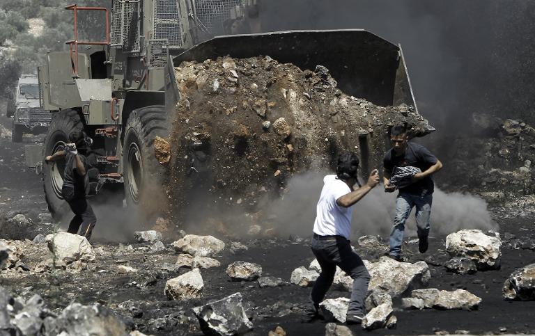 Người Palestine ném đá về phía máy xúc của Israel  trong một cuộc đụng độ sau hàng loạt vụ biểu tình chống lại việc trưng thu đất của người Palestine ở làng Kfar Qaddum, Palestin