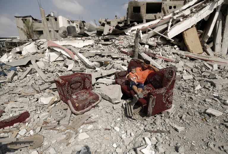 Người đàn ông Palestine và đứa con nhỏ ngồi trên chiếc ghế sofa giữa đống đổ nát của các tòa nhà bị phá hủy ở thành phố Gaza