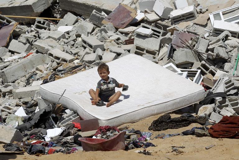 Một đứa trẻ Palestine ngồi trên tấm nệm giữa đống đổ nát của ngôi nhà bị trúng bom ở Abasan, ở Dải Gaza