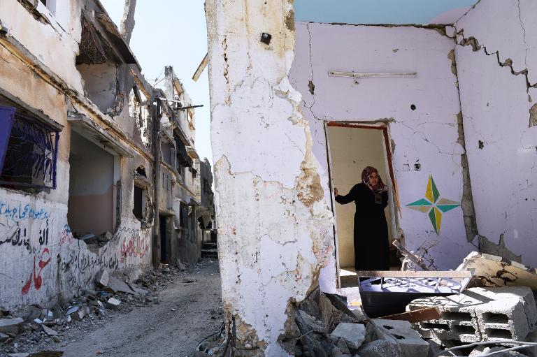 Người phụ nữ Palestine đứng trong khung cửa của một ngôi nhà bị hư hỏng hoàn toàn do đạn pháo