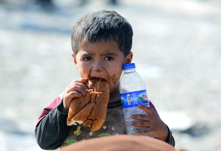 Một cậu bé Iraq đang ăn mẩu bánh mì và cầm chai nước khoáng khi cùng gia đình di chuyển qua biên giới Iraq-Syria tại Fishkhabur