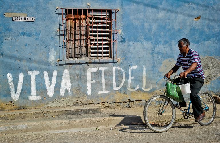 Một người đàn ông Cuba đạp xe ngang qua bức tường có dòng chữ graffiti ca ngợi cựu chủ tịch Cuba Fidel Castro tại thủ đô La Habana