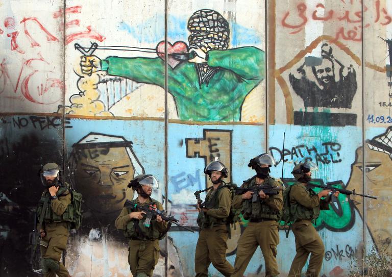 Binh sĩ Israel đứng trước bức tranh lớn được vẽ trên tường gần trạm kiểm soát Qalandiya giữa thành phố Bờ Tây Ramallah và Jerusalem