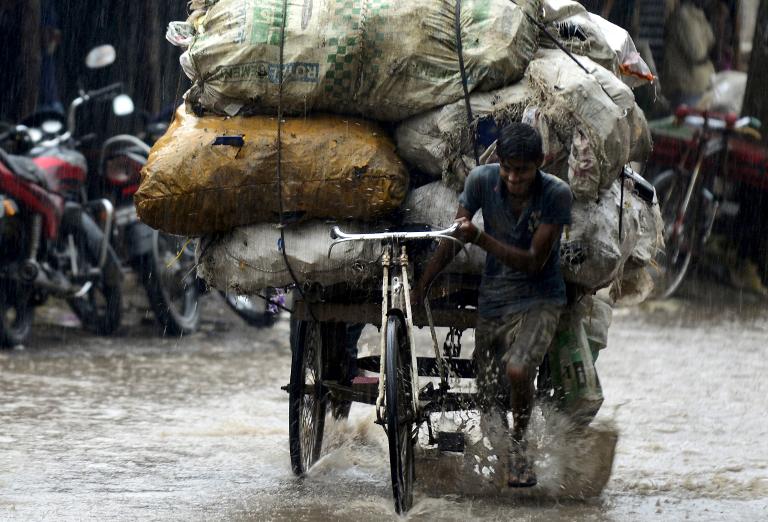 Người đan ông Bangladesh cố gắng kéo chiếc xe chờ đầy hàng hóa của mình giữa cơn mưa trong một con phố ngập lụt ở Dhaka, Bangladesh