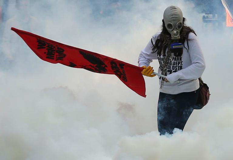 Một người biểu tình mang mặt nạ chống độc, cầm cờ giữa đám khói cay của cảnh sát chống bạo động ở thủ đô Ankara, Thổ Nhĩ Kỳ