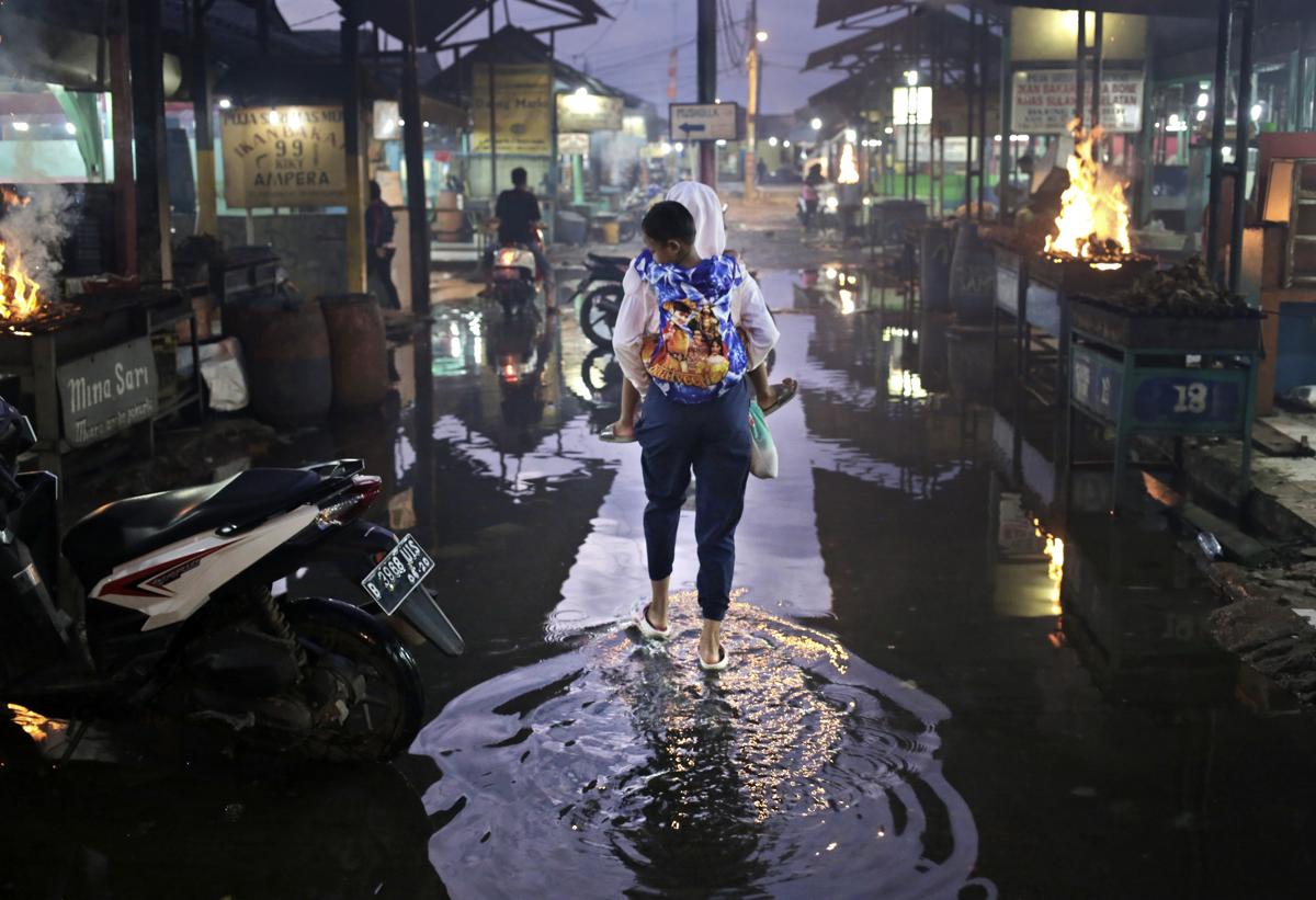 Một người phụ nữ cõng bé trai đi qua con hẻm ngập nước sau trận mưa lớn ở Jakarta, Indonesia, 26/02/2016.