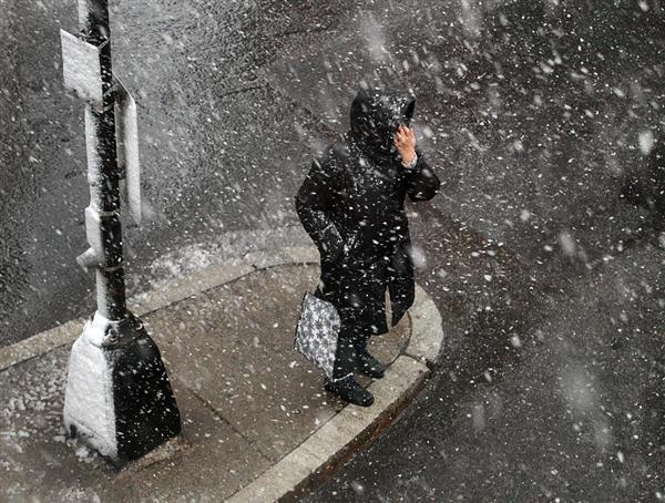  Một người phụ nữ đứng bên vệ đường khi ngoài trời tuyết đang rơi dày.