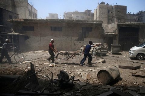 Hai người đàn ông vận chuyển thi thể một người bị trúng đạn từ cuộc không kích của quân chính phủ Syria ngày 25-7 tại Douma  gần Damascus, thuộc vùng kiểm soát của phiến quân Syria - Ảnh: Reuters