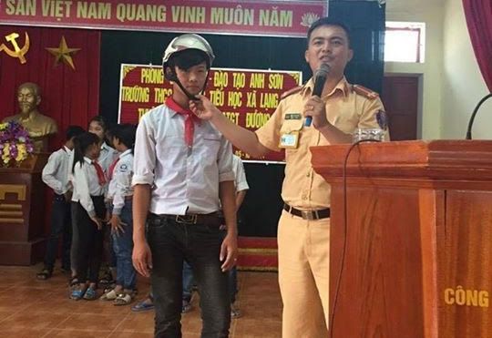Cán bộ CSGT Công an huyện Anh Sơn hướng dẫn học sinh đội mũ bảo hiểm đúng cách