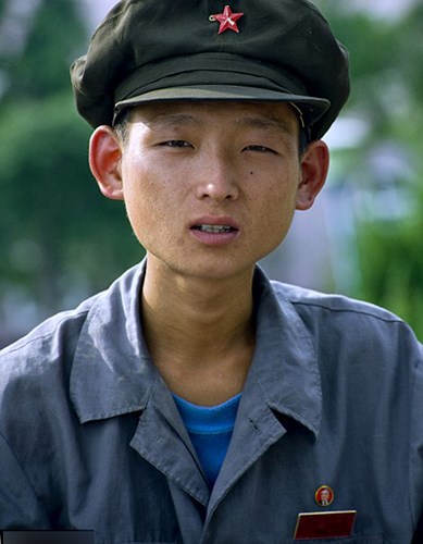 Một nam giới đội mũ lưỡi trai đặc trưng ở Triều Tiên và đeo huy hiệu có hình lãnh tụ Kim Nhật Thành.