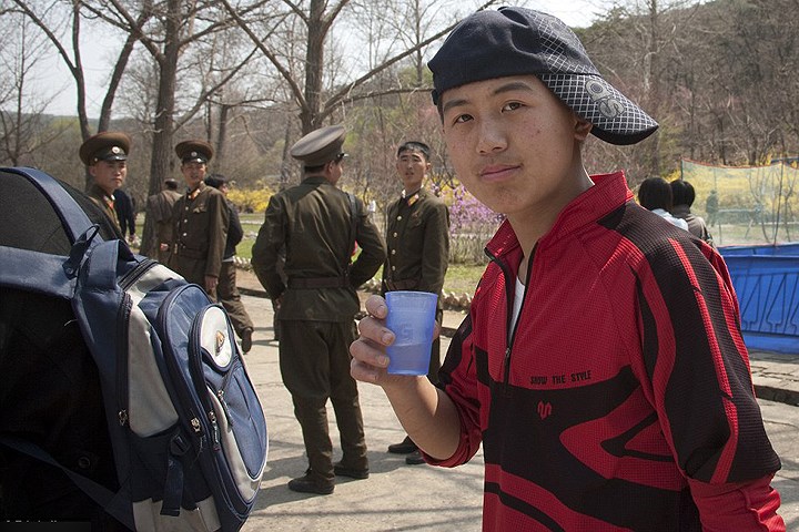 Một thiếu niên Triều Tiên đội ngược mũ bóng chày khi đứng gần những người lính Triều Tiên.