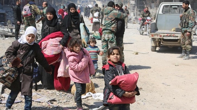 Các em nhỏ ôm theo đồ đạc di chuyển trên đường phố Đông Ghouta. Ảnh: Reuters