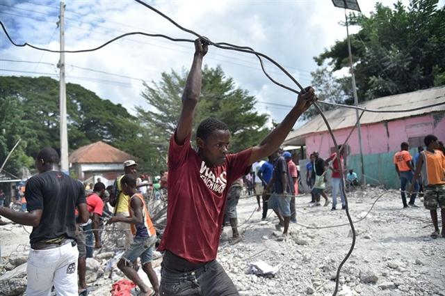 Người dân Haiti đi thu lượm những mảnh sắt vụn từ một công trình vừa bị phá hủy trong trận động đất ở miền bắc Haiti ngày 7/10. Ảnh: AFP