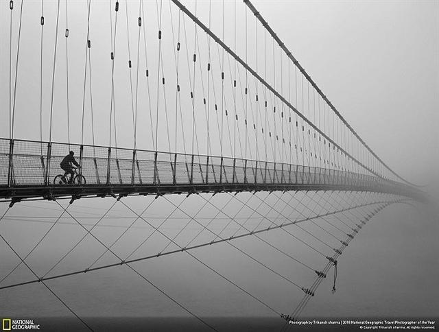 Giải ảnh bình chọn, mục Đô thị: “Du hành đến thiên đường” - Trikansh Sharma. “Một lữ khách đang đạp xe trên cầu Ram Jhula, Ấn Độ. Không thấy điểm kết thúc của cây cầu như thể người đàn ông đang du hành đến thiên đường vậy.” (Ảnh: National Geographic)