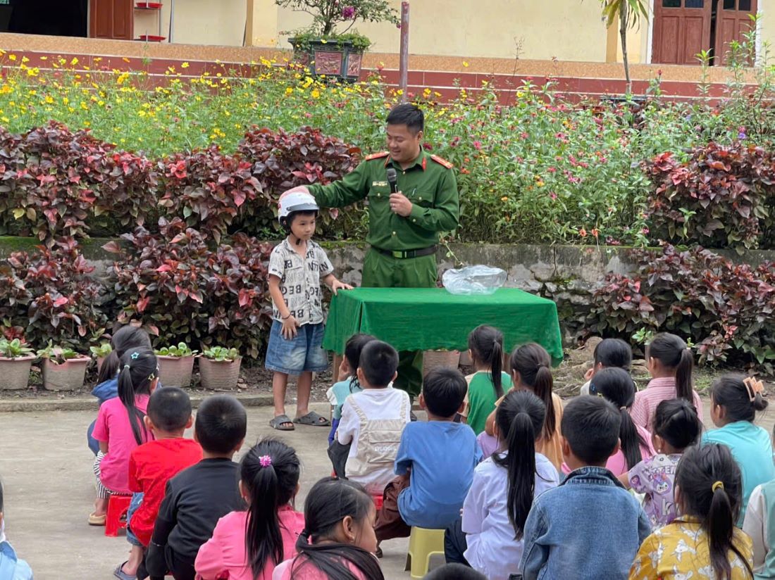 Cán bộ Công an xã Bình Chuẩn hướng dẫn học sinh đội mũ bảo hiểm đúng cách