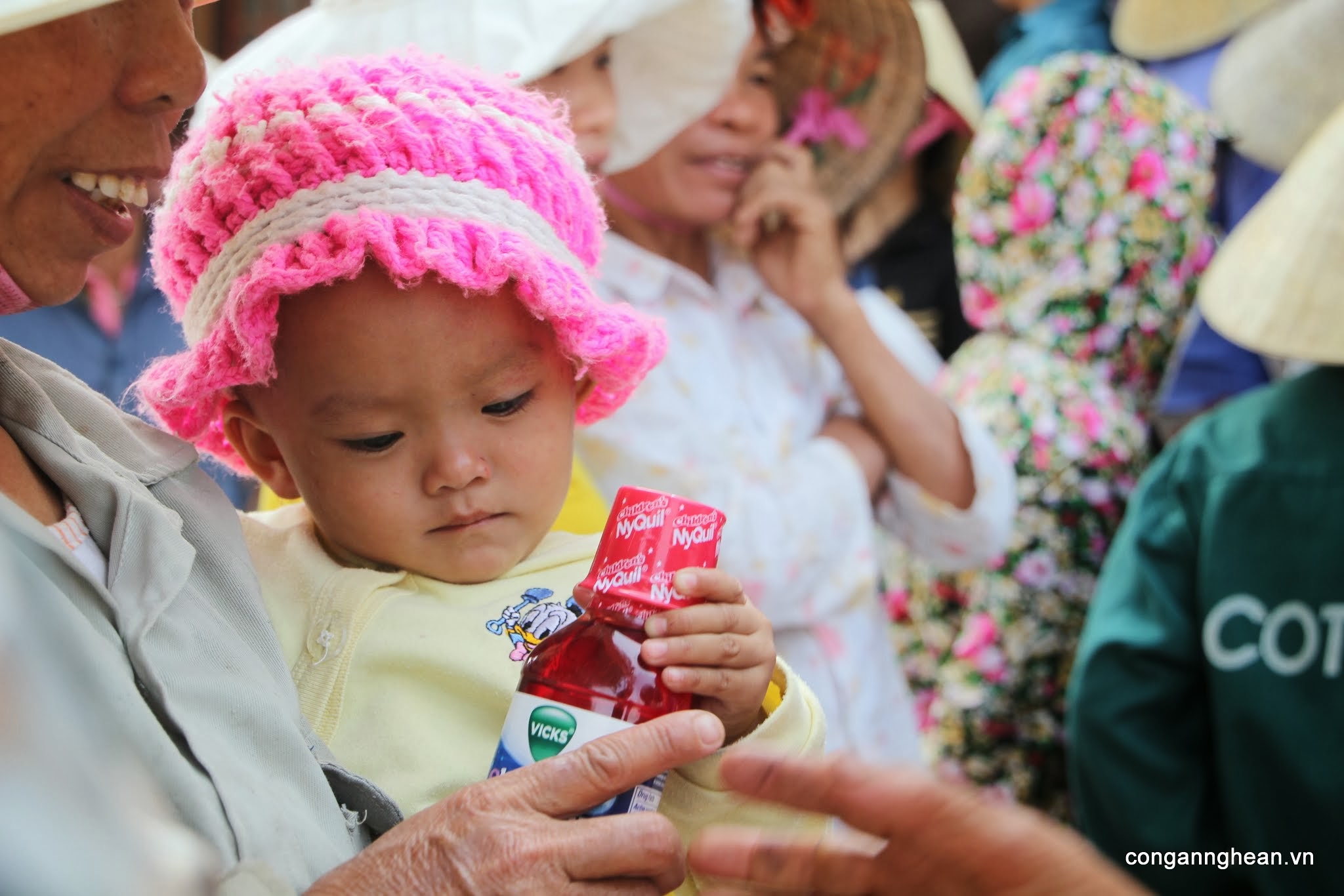 Bé gái mới 9 tháng tuổi cầm một chai siro chữa ho vừa được tặng. Bé còn nhỏ, tay chưa đủ lực nên mẹ phải đỡ giúp bé 
