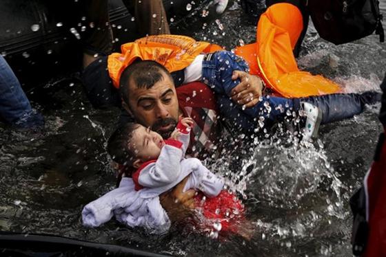 Một người tị nạn Syria ôm chặt hai con khi cố gắng rời khỏi chiếc xuồng tới quần đảo Lesbos, Hy Lạp.
